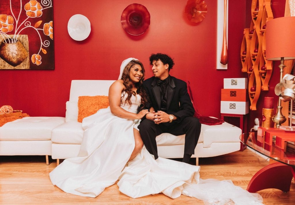 Bride and groom sitting on couch for couples portrait. Looking at each other smiling