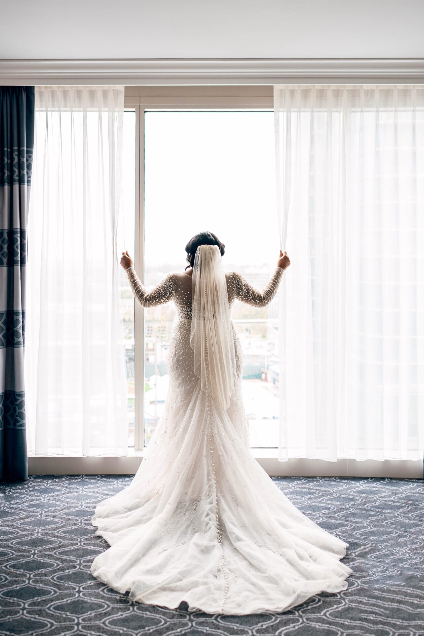 Bride in wedding dress looking out window at Kimpton Tryon Park hotel