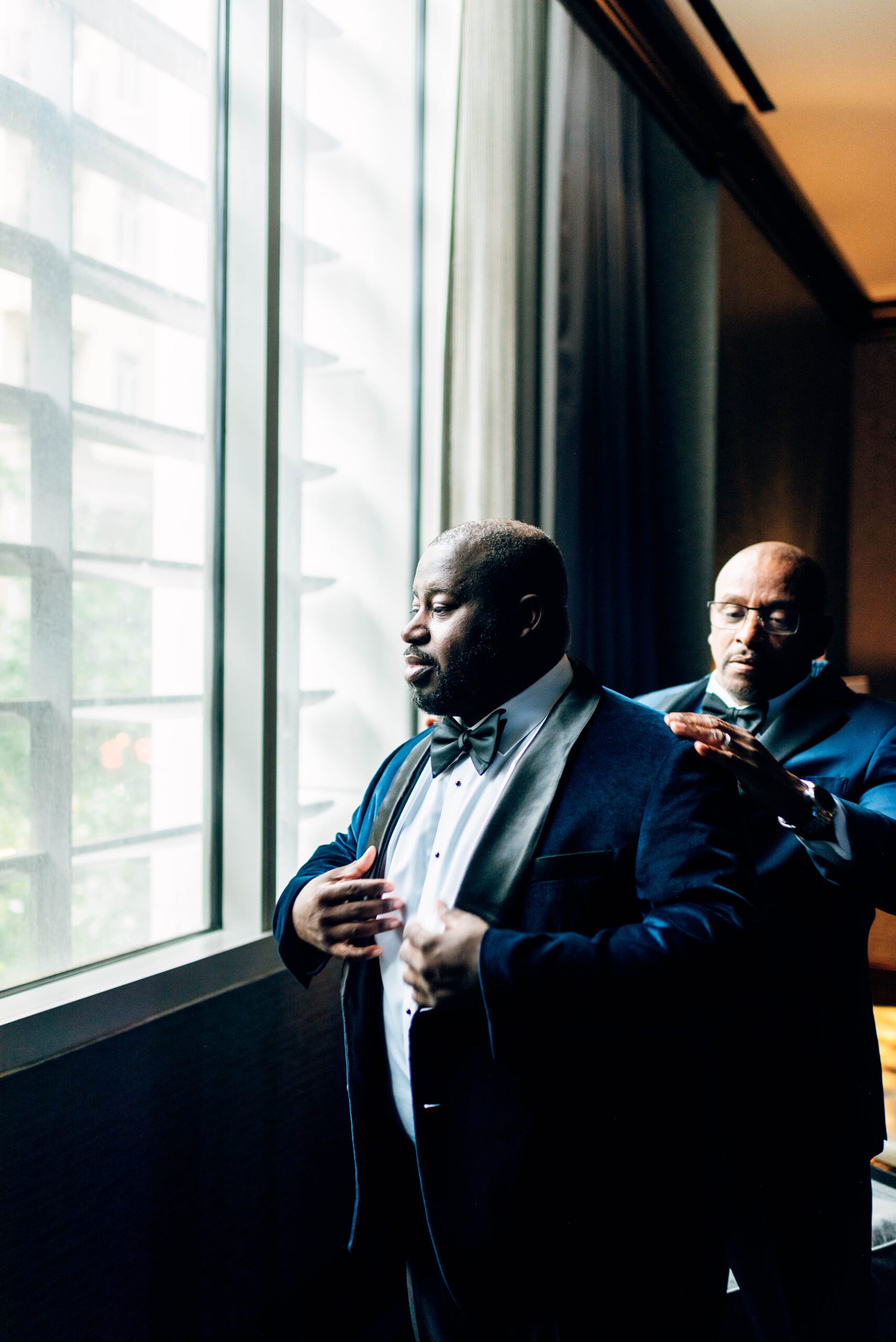 Groom getting ready at Kimpton Tryon Park hotel by window with the help of his best man