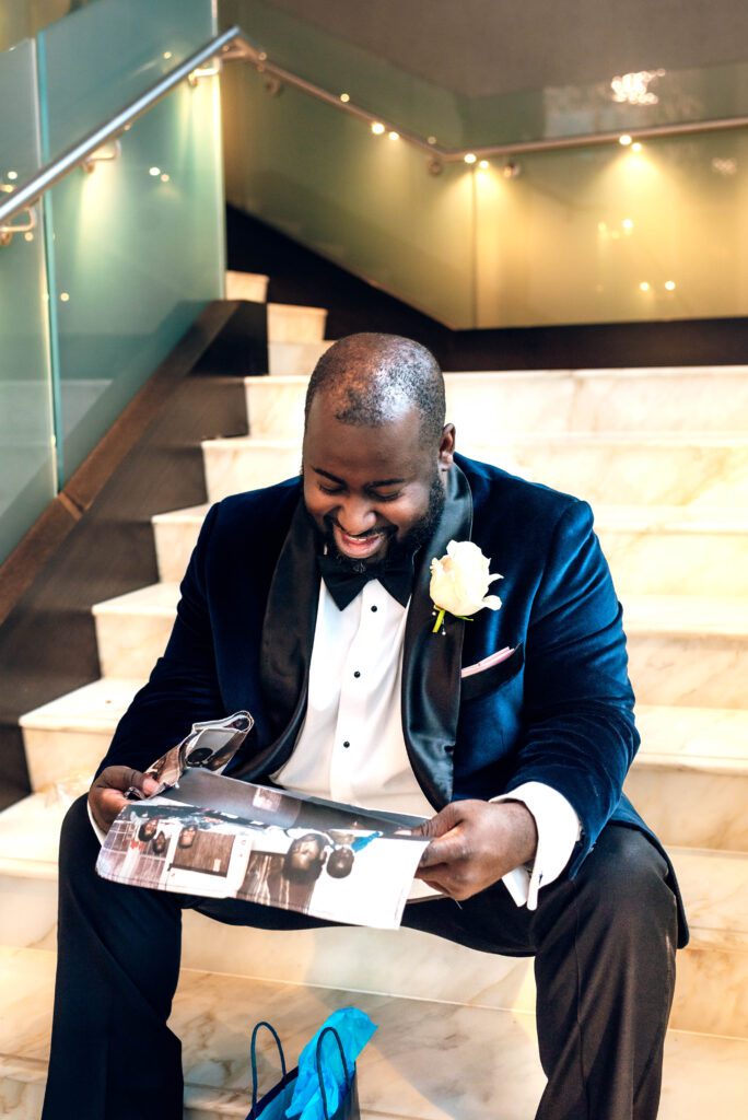 Groom sitting on steps looking at gift from Bride in Kimpton Tryon Park hotel