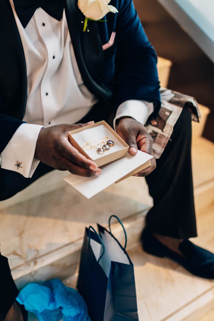 Groom sitting on steps looking at gift from Bride in Kimpton Tryon Park hotel