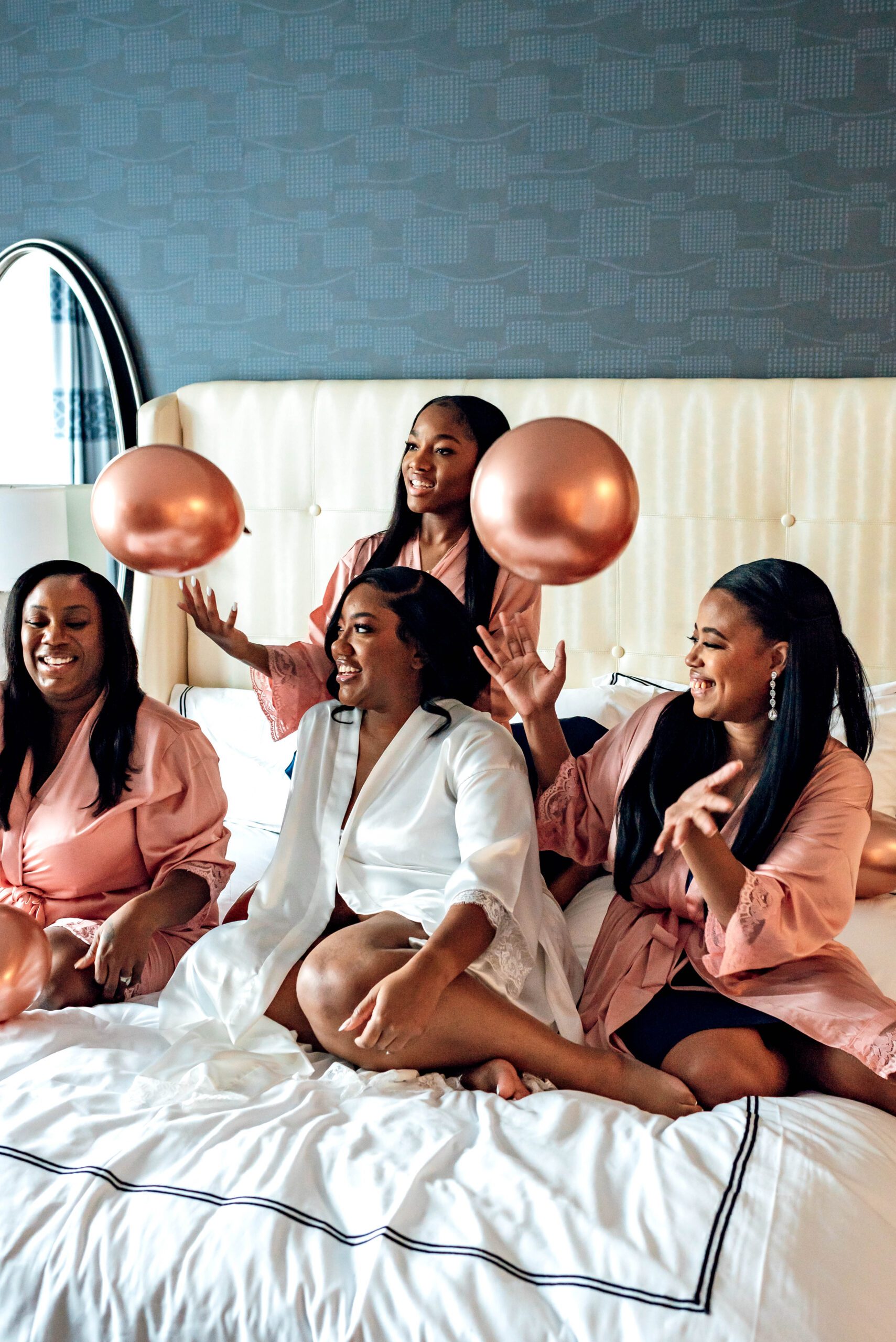 Bride and bridesmaids throwing balloons in hotel room in matching robes before getting ready for the wedding