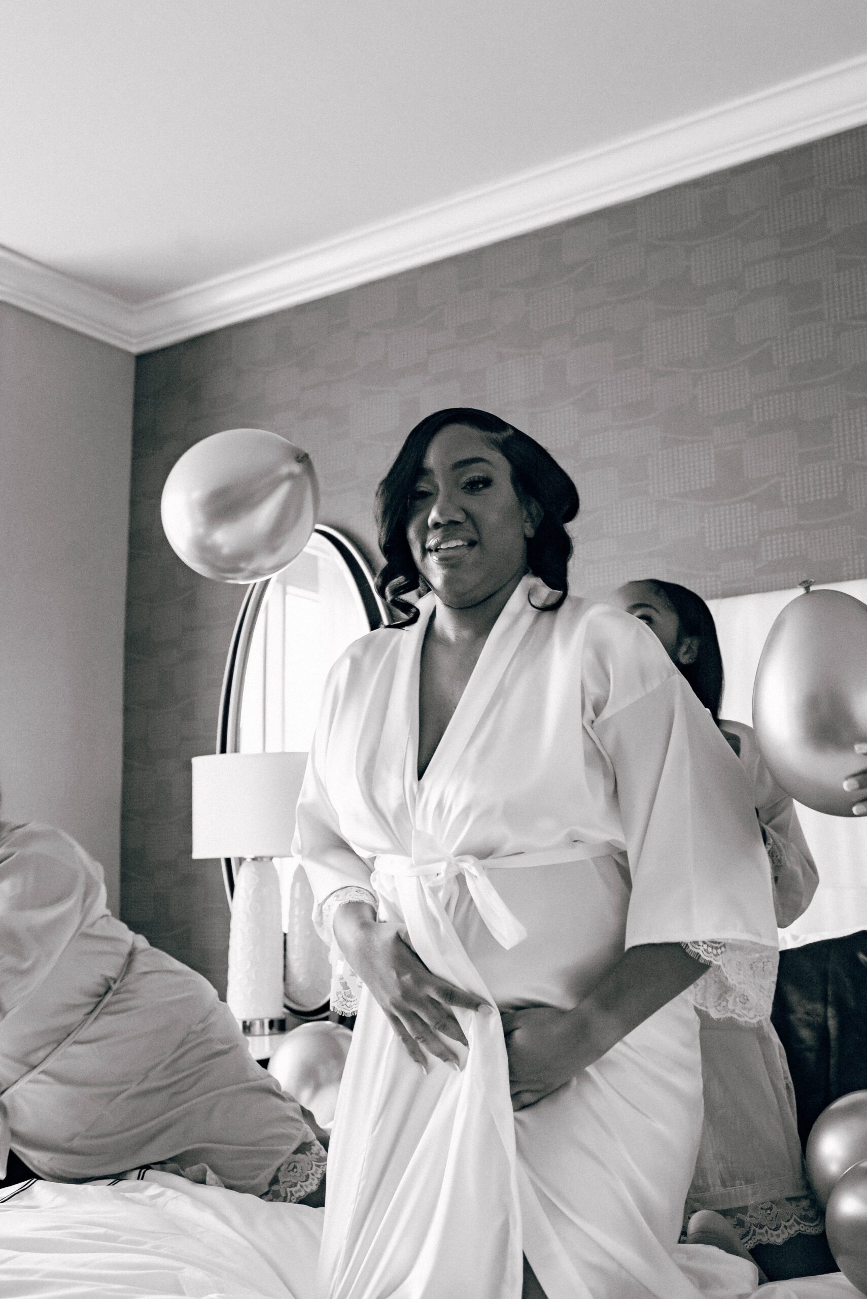 Bride and bridesmaids throwing balloons in hotel room in matching robes before getting ready for the wedding
